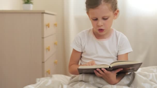 漂亮的女孩看书 早上坐在她的床上 生活方式和童年的概念 — 图库视频影像