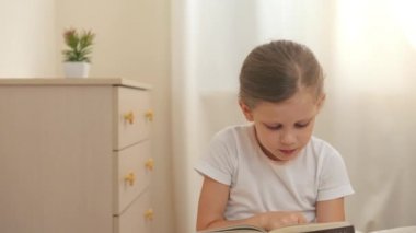 Sevimli küçük kız hikaye kitabı holding, yatağın üzerine oturan ve okuma.