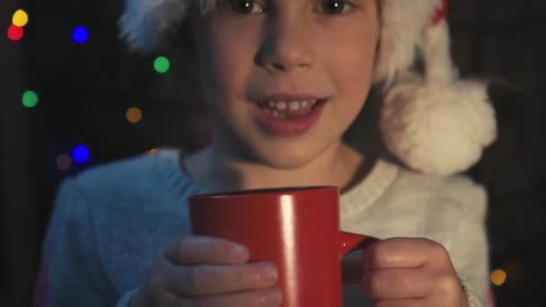 Χαριτωμένο Παιδί Καπέλο Santa Κρατώντας Ερυθρό Κύπελλο Και Πίνοντας Καυτό — Αρχείο Βίντεο