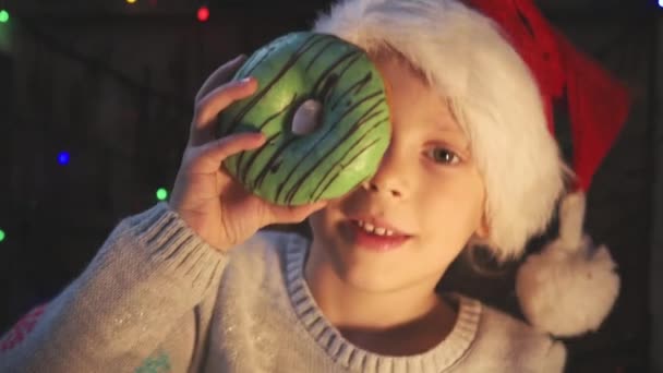緑のドーナツを持ってサンタ帽子の愛らしい少女 冬の休日 冬の祭典コンセプト — ストック動画