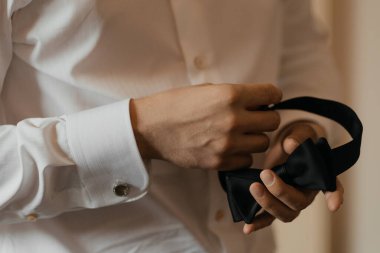 Beyaz gömlekli şık bir adam smokinli klasik bir siyah papyon tutuyor. Minimalist moda kavramı.