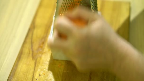 Moliendo zanahorias en un rallador. Tablero de madera en la mesa de la cocina . — Vídeos de Stock