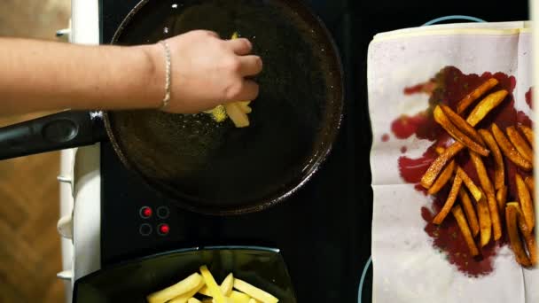 Primo piano di mani che preparano patatine fritte. Le patate affettate sono fritte in olio in una padella per friggere. Una nuova porzione . — Video Stock