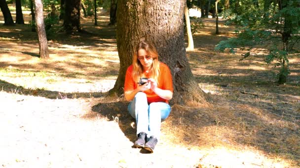 Bir park. Kız bir ağacın altında oturuyor. Konuşuyor ve gülümsüyor. — Stok video