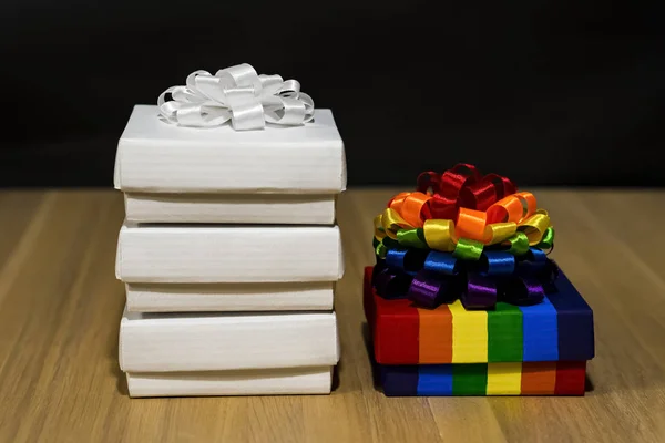 Geschenkkomposition. Schachtel mit Streifen in verschiedenen Farben. Vielfarbige Schleife. In der Nähe befinden sich weiße Boxen. Holztisch. — Stockfoto