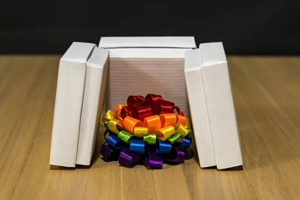 Composición del regalo. Caja con rayas de diferentes colores. Arco multicolor. Hay cajas blancas alrededor. Mesa de madera . —  Fotos de Stock