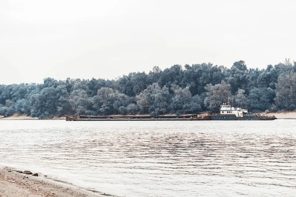 A cargo ship is moving along the river. Lush greenery along the shore.