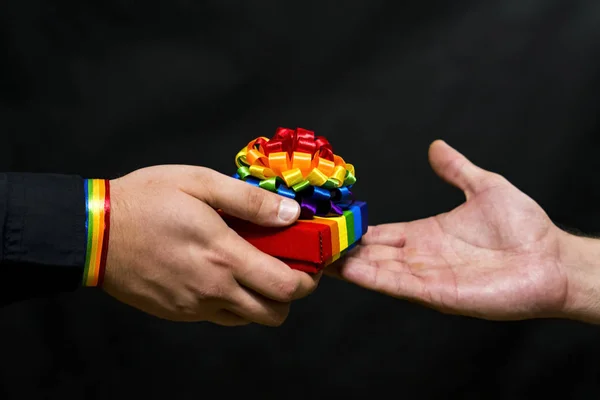 Comunidad LGBT. Un regalo festivo con símbolos se pasa de mano en mano. Fondo oscuro . —  Fotos de Stock