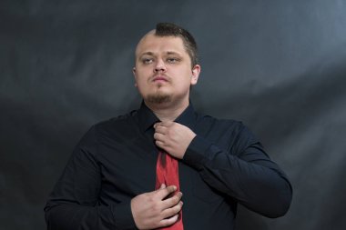 Punk içinde karanlık bir gömlek. Kırmızı kravat düzeltiyor. Ciddi ve memnun yüzüdür.