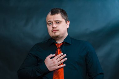 Punk içinde karanlık bir gömlek. Kırmızı kravat. Ciddi ve şüphe gölgesi ile yüzüdür. Sağ eliyle dokunduğu kravatını kumaş.