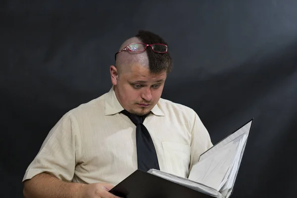 Punk está leyendo un registro de trabajo. Las gafas se movían en la frente. Camisa blanca, corbata oscura. En la cara una expresión de duda y malentendido . — Foto de Stock
