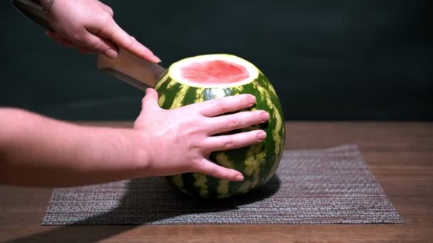 Watermelon is cut into slices with a knife. Wooden table. One red slice lays nearby. — Stock Video