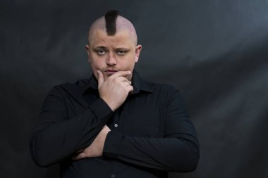 Siyah gömlekli bir mohawk ile punk. Dalgınlık yüz ifadesidir. Sol el çeneye dokunan.