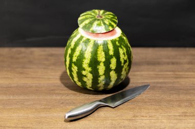 Karpuz ahşap bir masa üzerinde. Karpuz yanındaki bıçağınızdır. Meyve üst kısmı kesilmiş.