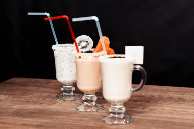 Ahşap bir masa üzerinde bardaklarda güler yüzlü. Siyah arka plan. Gözlük kenarları kivi, karpuz ve ananas dilimleri vardır.