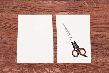 Makas ve beyaz bir levha yarıya. Pembemsi kahverengi ahşap arka plan.