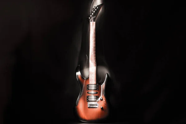 Electric guitar with six strings. Dark background.
