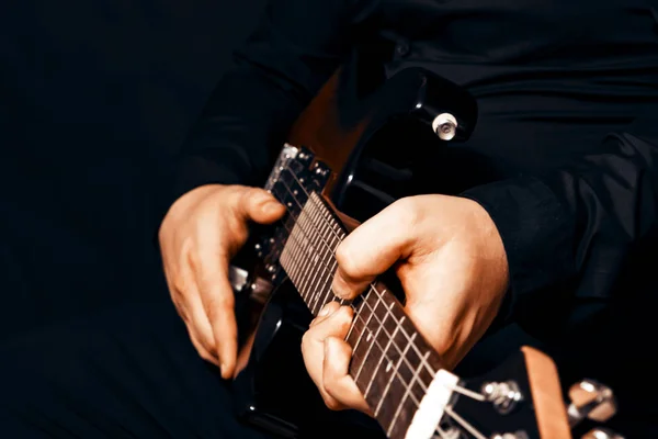 The fingers of the musician touch the strings of a six-string electric guitar. Dark background.