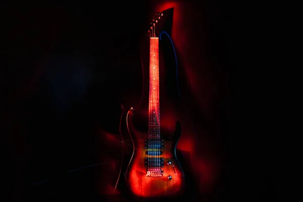 Guitarra eléctrica en los rayos de rojo sobre un fondo oscuro. Efecto luz . —  Fotos de Stock