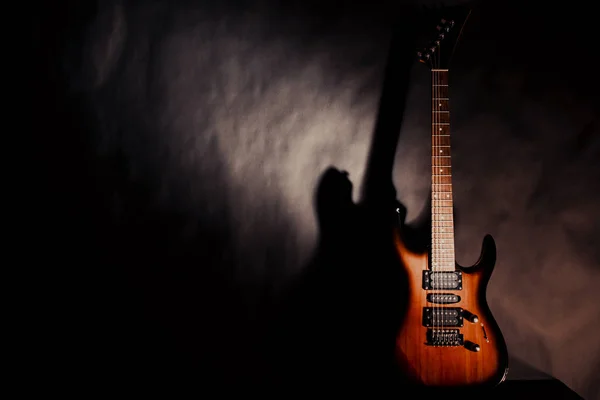Guitarra eléctrica sobre fondo oscuro. La sombra de la guitarra en la pared . —  Fotos de Stock