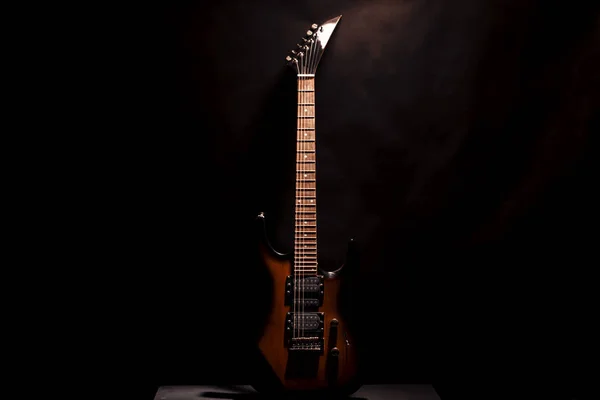 Red electric guitar on a dark background. Located vertically on a wooden table.