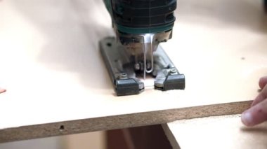 El ile elektrikli perde testere ile çalışır. Kesim masası tamamlanması. Görünür küçük ahşap tıraş.