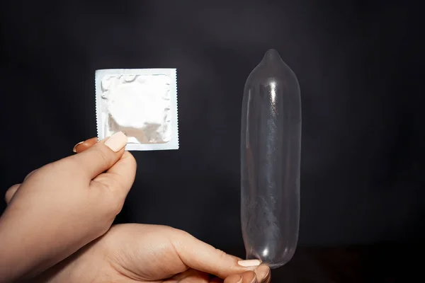 Preservativo na mão de uma rapariga. inflar. Bactérias negras . — Fotografia de Stock