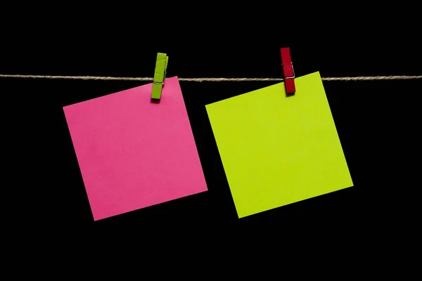 Copiar espacio. Fondo negro. Hojas de papel amarillas y rosadas cuelgan de una cuerda . — Foto de Stock