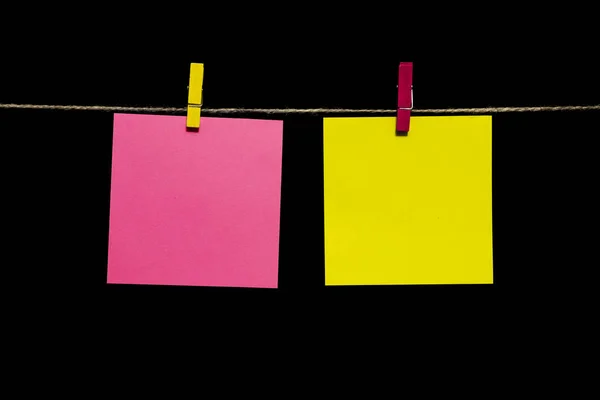 Copiar espacio. Dos hojas de papel amarillo y rosa con pinzas de ropa cuelgan de una cuerda . — Foto de Stock
