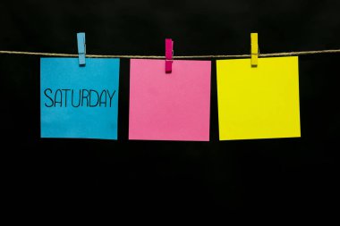 Uzay kopyalayın. Cumartesi. Not masmavi bir etiket üzerine yazılmıştır. Üç renkli kağıda bir ip clothespins bağlı.