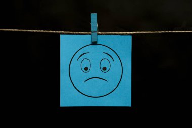 Uzay kopyalayın. Bir surat ile mavi etiket. Hayal kırıklığı yüz ifadesi. Kağıdın bir clothespin iple bağlı olduğu.