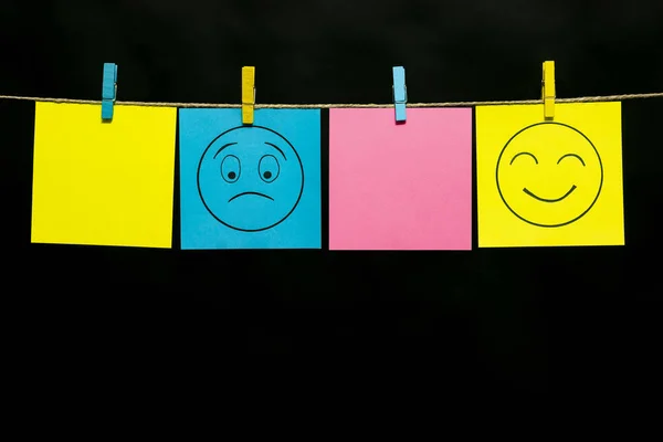 Copy space. Four stickers. On two sheets a smileys face with an expression of puzzled and gaiety. Stickers are attached to the rope with clothespins.