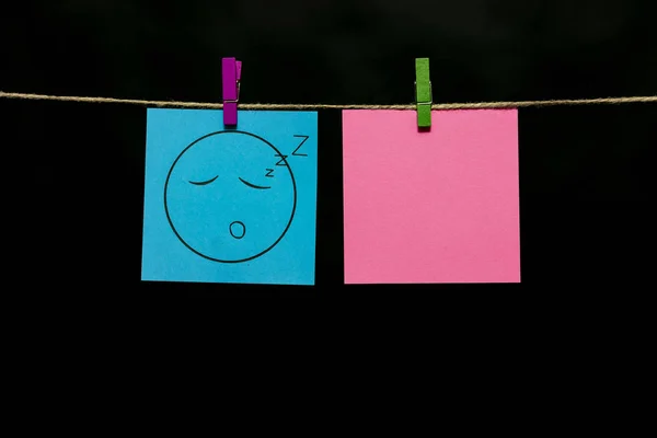 Copy space. Two stickers. On azure page smiley. Deep sleep. Stickers are attached to the rope with clothespins.
