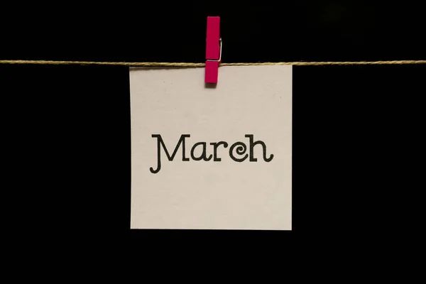 Kopieer ruimte. Maand van het jaar. Witte sticker. Op het blad inscriptie maart. Het blad is gekoppeld aan het touw met wasknijper. — Stockfoto