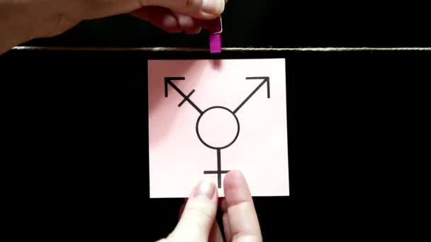 På det vita arket är bild av transpersoner symbol. Plåten fästes manuellt med en klädnypa på repet. — Stockvideo