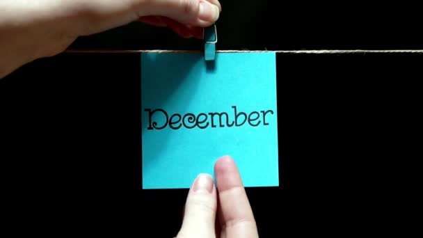 Monat des Jahres. blaue Plakette. auf dem Blatt Aufschrift Dezember. das Laken wird manuell mit einer Wäscheklammer am Seil befestigt. — Stockvideo