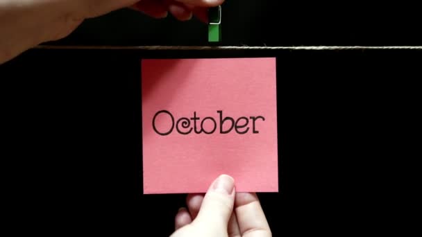 Maand van het jaar. Winter. Op het blad inscriptie oktober. Roze sticker. Het blad is handmatig gekoppeld met een wasknijper op het touw. — Stockvideo