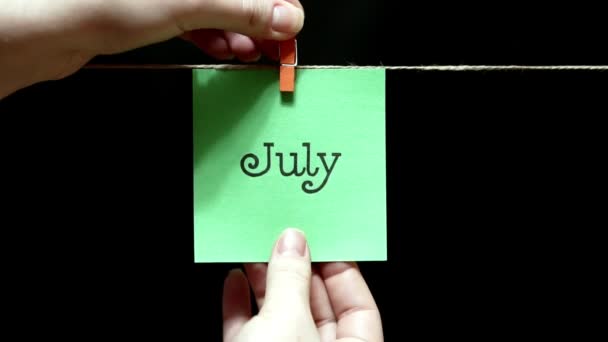 Monat des Jahres. Sommer. auf dem Blatt Beschriftung Juli. das Laken wird manuell mit einer Wäscheklammer am Seil befestigt. — Stockvideo