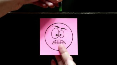 Copy space. Pink sticker with a facial expression of anger. The sheet is attached manually with a clothespin on the rope.