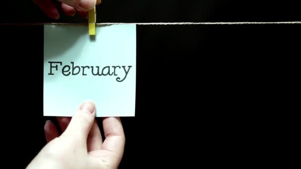 Two multicolored stickers. On left a sheet inscription February. On the right white a sheet an expression of festive mood. Black background. — Stock Video