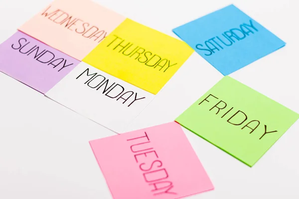 Folhas de papel em cores diferentes são dispostas na forma de uma seta. Pedaço de papel tem o nome de um dia da semana escrito nele. — Fotografia de Stock