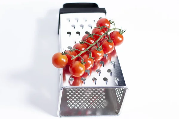 La râpe de cuisine à quatre côtés repose sur une surface blanche. Sur elle est un bouquet de tomates cerises fraîches. — Photo