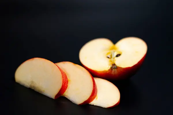 No centro da tela estão fatias fatiadas e metade de uma maçã suculenta vermelha. Fundo escuro. — Fotografia de Stock