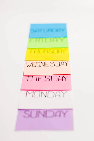 Sheets of paper of different colors are arranged in a straight line. Each piece of paper has the name of one day of the week written on it. — Stock Photo, Image