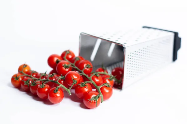 Four-sided kitchen grater lies on a white surface. Nearby is a bunch of fresh cherry tomatoes. — Stock Photo, Image