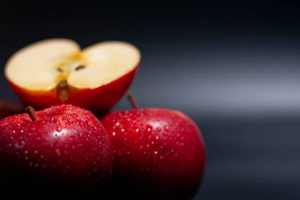 No canto inferior esquerdo, duas maçãs vermelhas inteiras estão em uma superfície escura. Em cima está metade de uma fruta.. — Fotografia de Stock