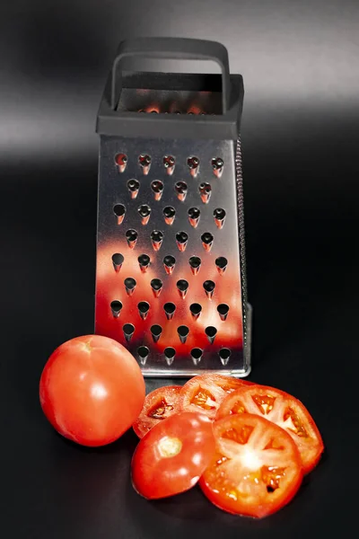 Râpe de cuisine à quatre côtés. Il y a une tomate rouge fraîche et plusieurs tranches de tomate tranchée à proximité. — Photo