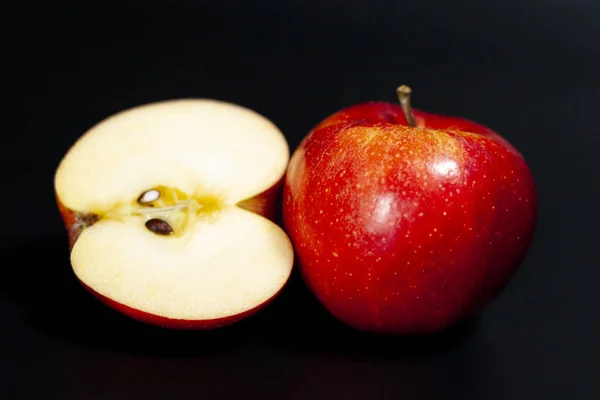 No centro da tela está toda uma maçã suculenta vermelha e metade da mesma. Fundo escuro. Fechar.. — Fotografia de Stock