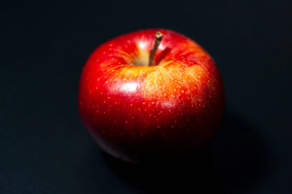 Czerwone jabłko na ciemnym tle. Świeża łodyga jest skierowana w stronę soczewki.. — Zdjęcie stockowe