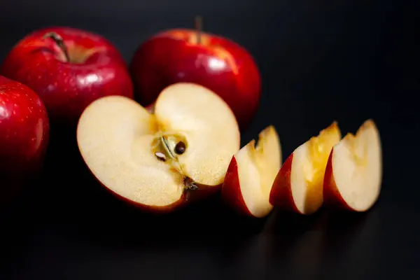 No centro da tela estão fatias fatiadas e metade de uma maçã suculenta vermelha. Acima estão frutos inteiros. Fundo escuro. — Fotografia de Stock